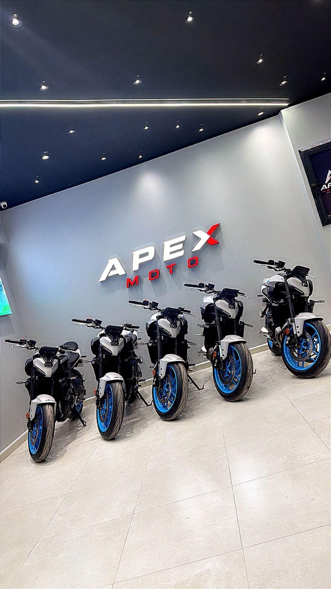 Motos alignées dans le showroom APEX MOTO, devant le logo lumineux
